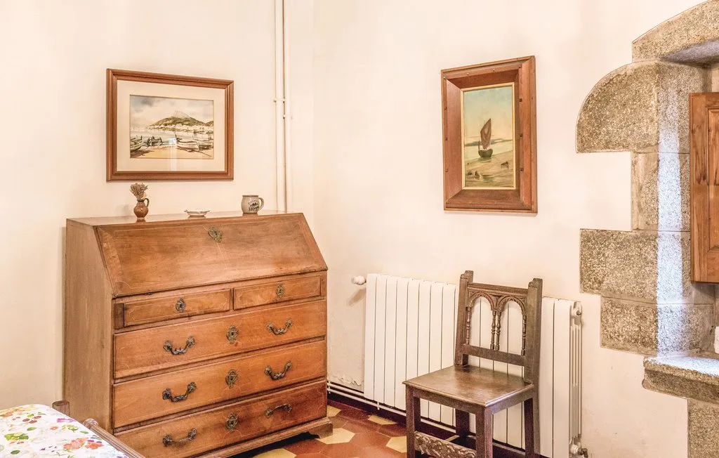 Un dormitorio con una cómoda de madera, cuadros enmarcados y un radiador.
