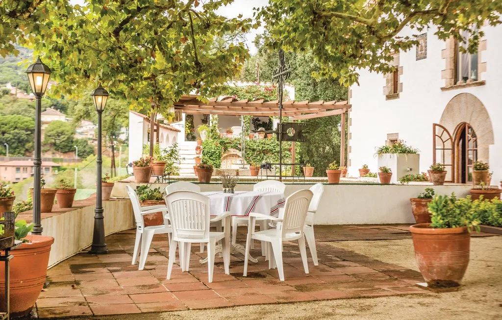 Un patio comedor al aire libre con asientos blancos bajo una pérgola frondosa.