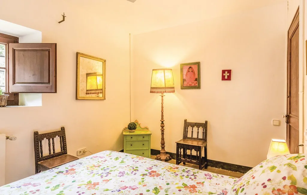 Un dormitorio con ropa de cama floral, asientos de madera y una lámpara de pie encendida.