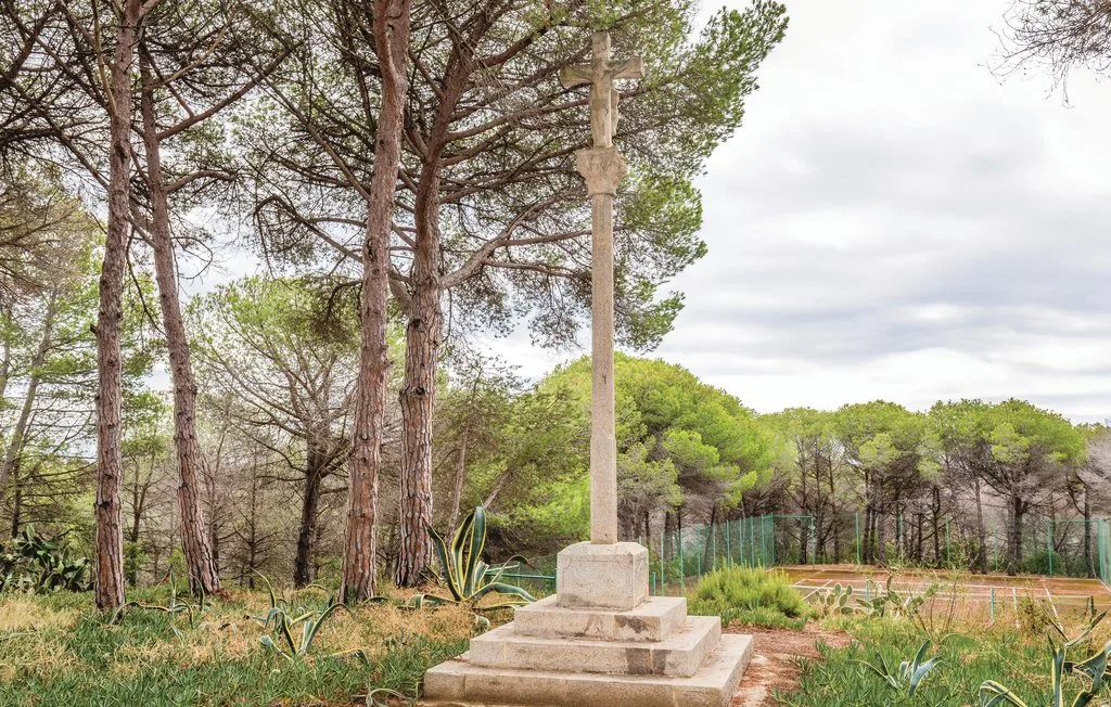 Una cruz de piedra se alza entre árboles y vegetación baja.