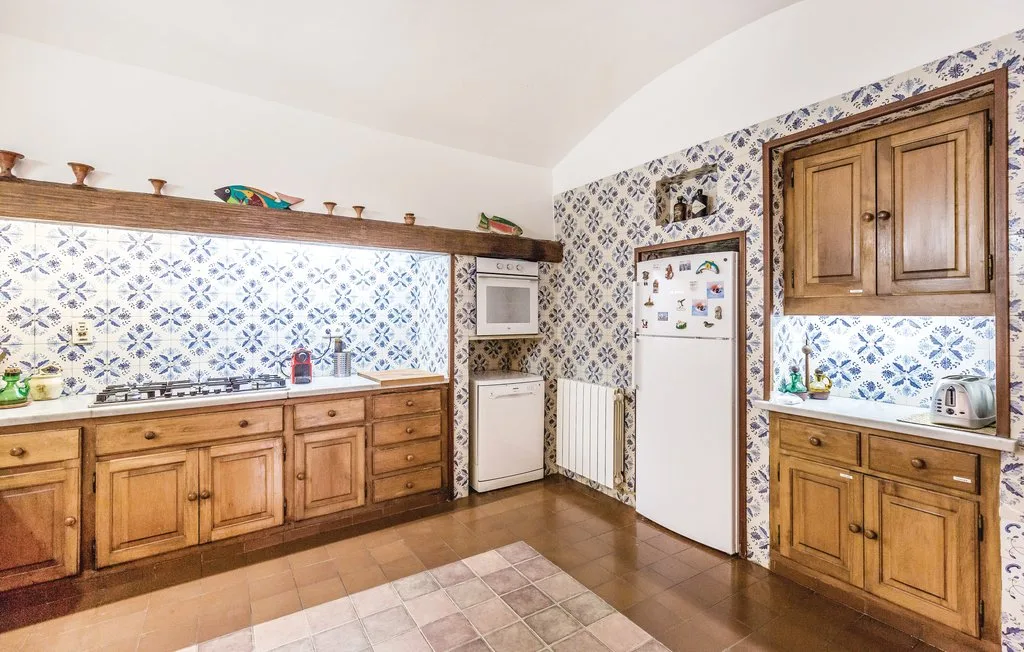 Una cocina alicatada con armarios de madera, un refrigerador y electrodomésticos sobre la encimera.