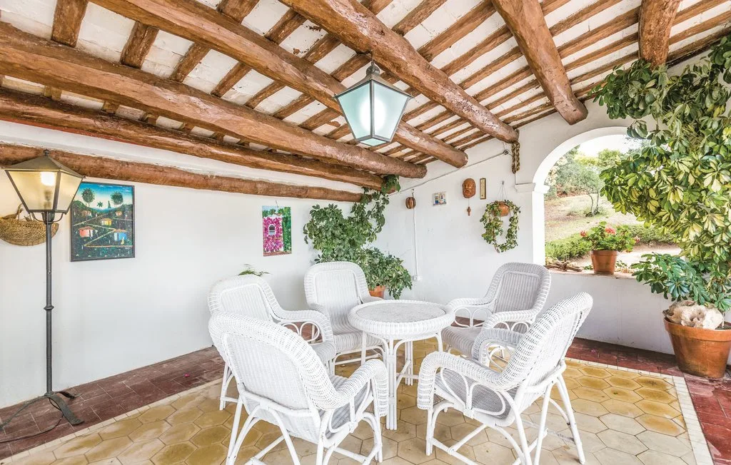 Un patio cubierto con asientos blancos alrededor de una mesa pequeña y plantas.
