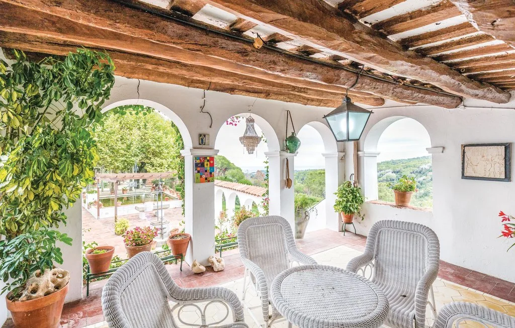 Una terraza cubierta con arcos y asientos de mimbre con vistas a un paisaje verde.