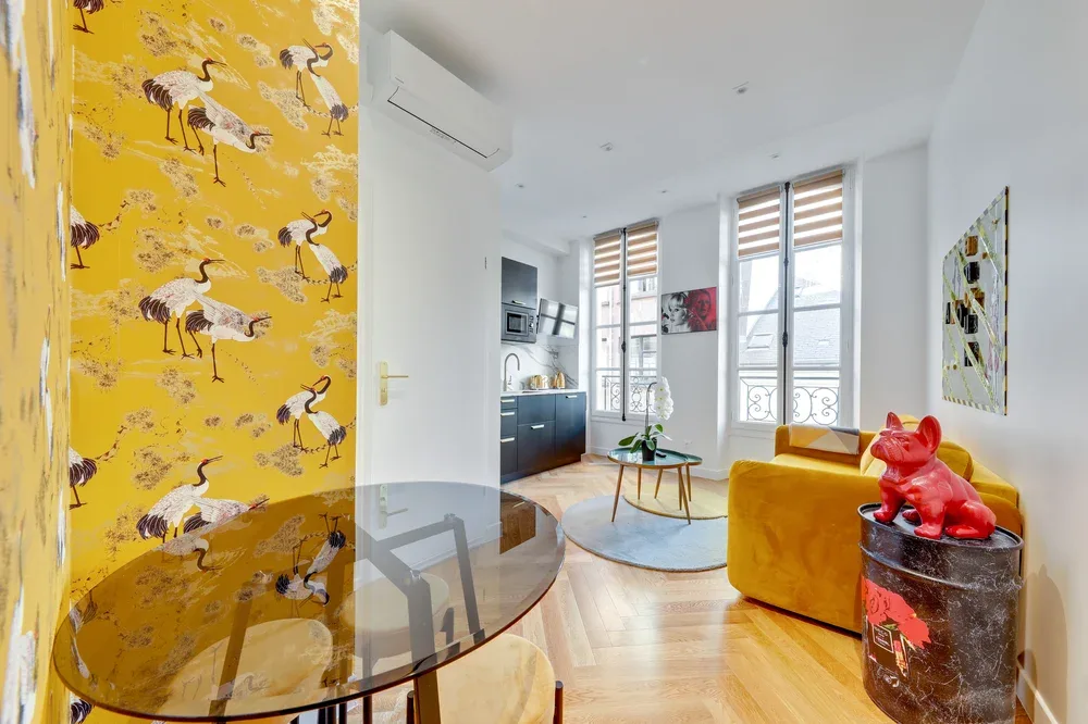 Una luminosa sala de estar con un sofá amarillo y ventanas altas.