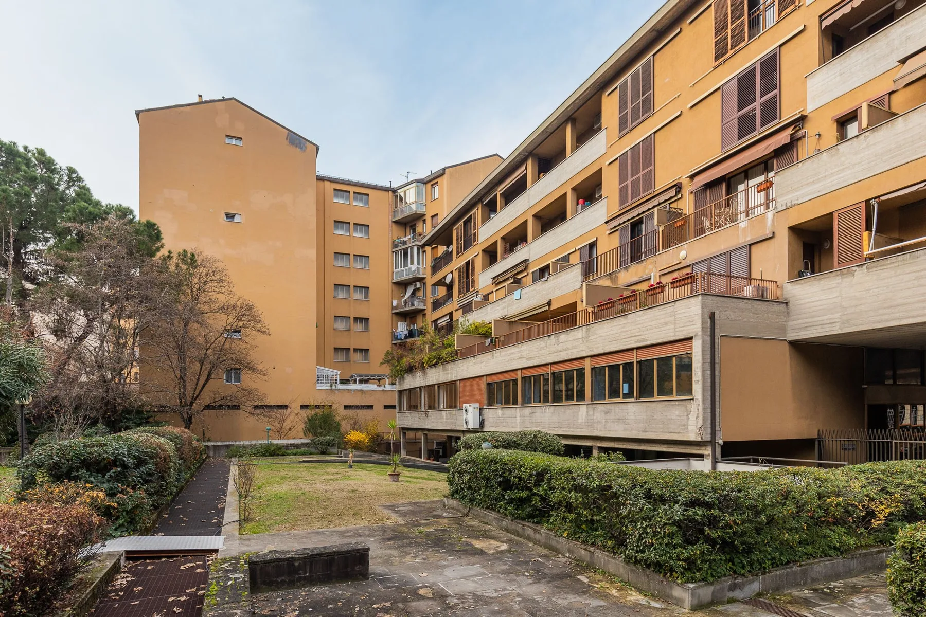 An apartment building surrounds a landscaped courtyard with paved paths and shrubs.