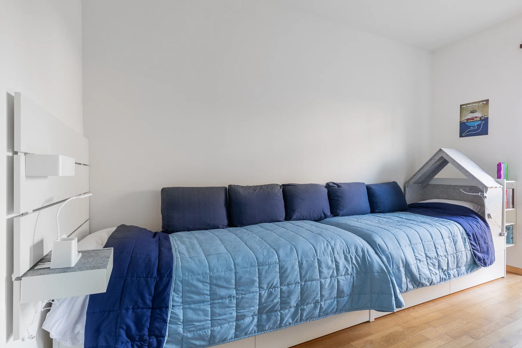 A bedroom with a long bed covered by a blue quilt.