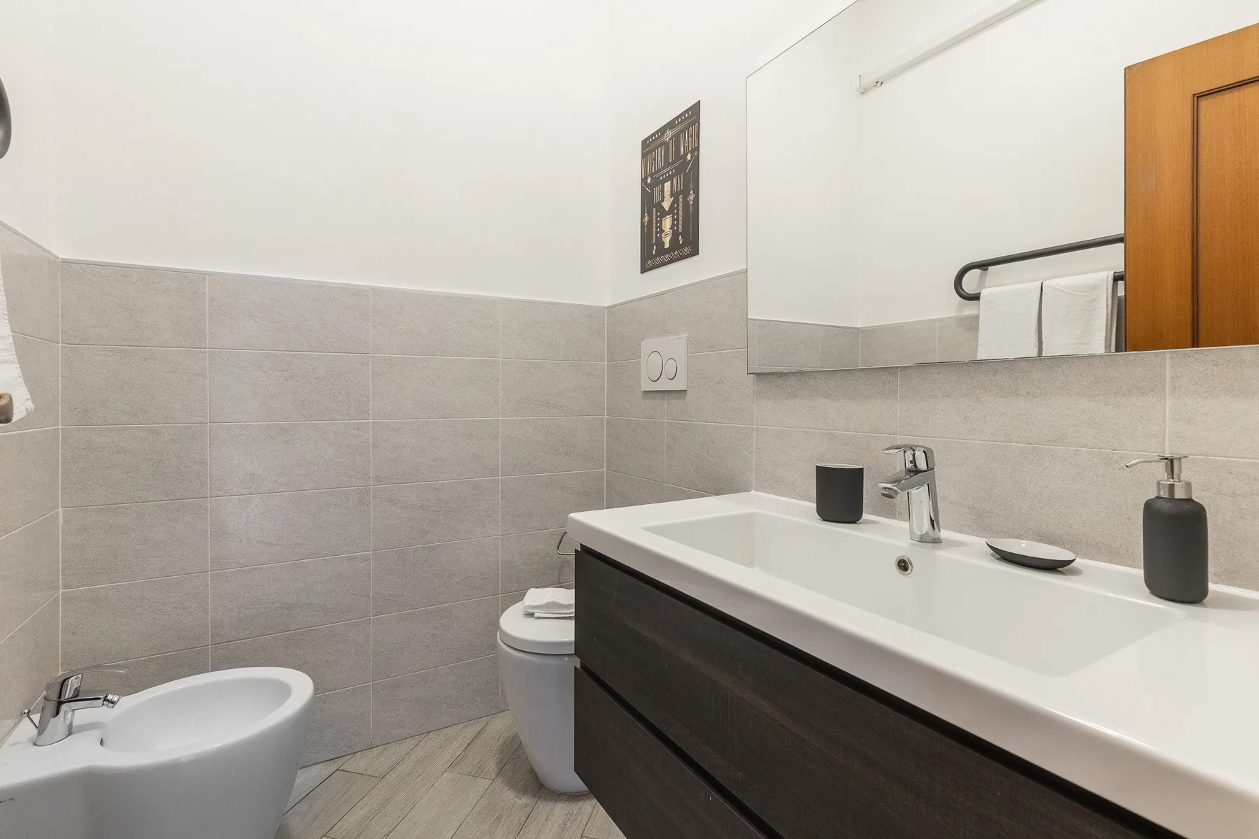 A tiled bathroom with a long vanity, sink, toilet, and bidet.