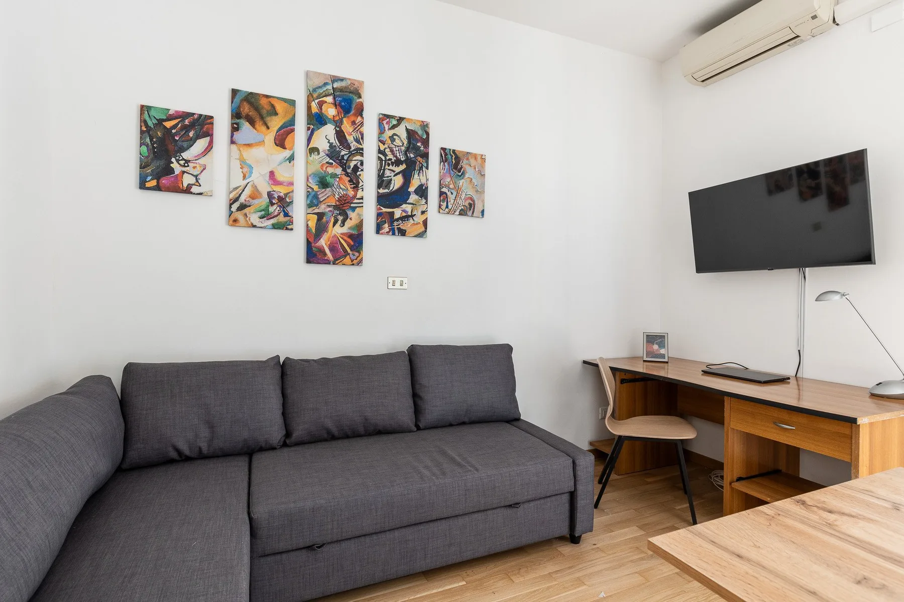 A living room with a gray sectional sofa, colorful wall art, and a desk.