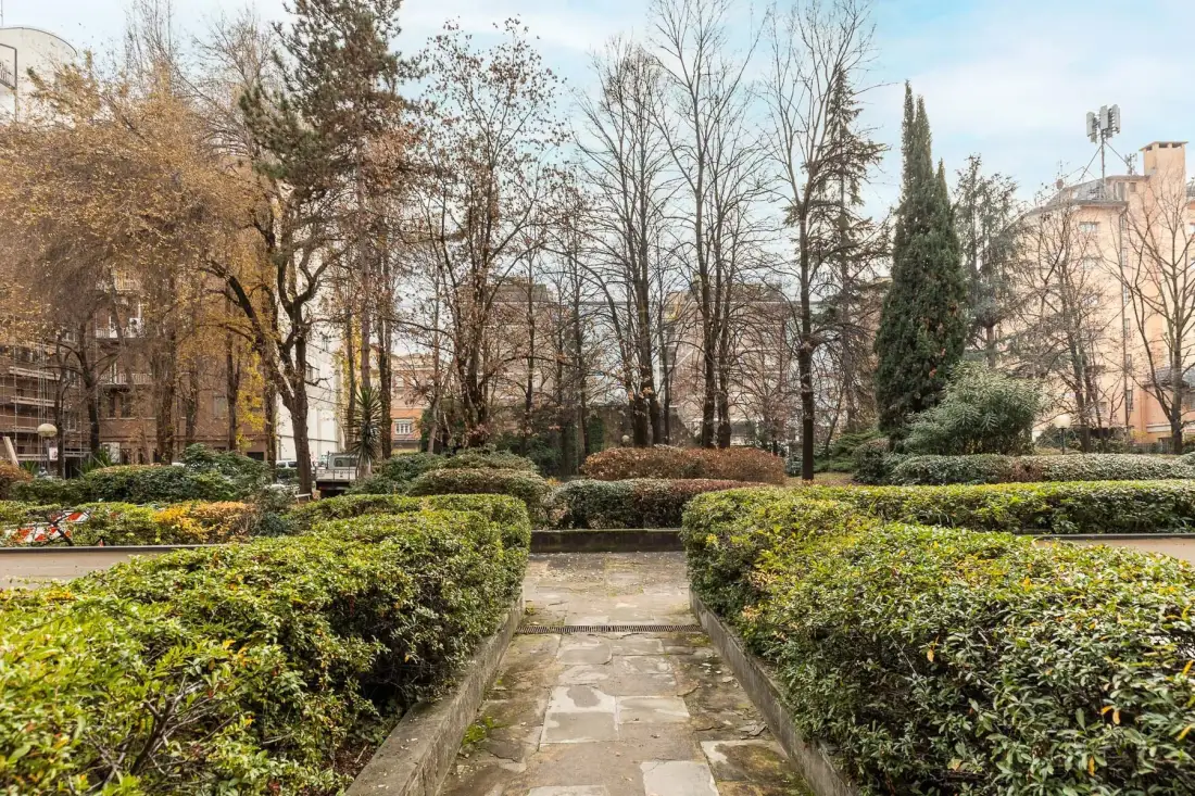 A stone walkway runs between trimmed hedges in a landscaped garden.