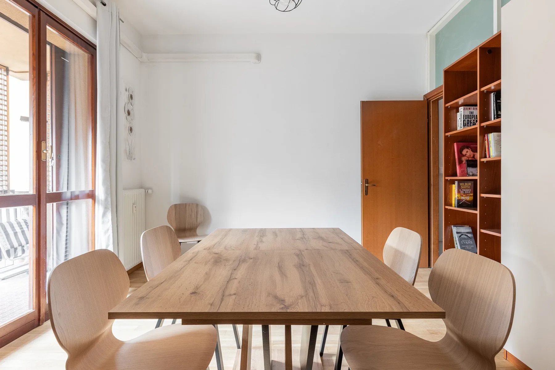 A dining area with a long wooden table and chairs beside a glass door.