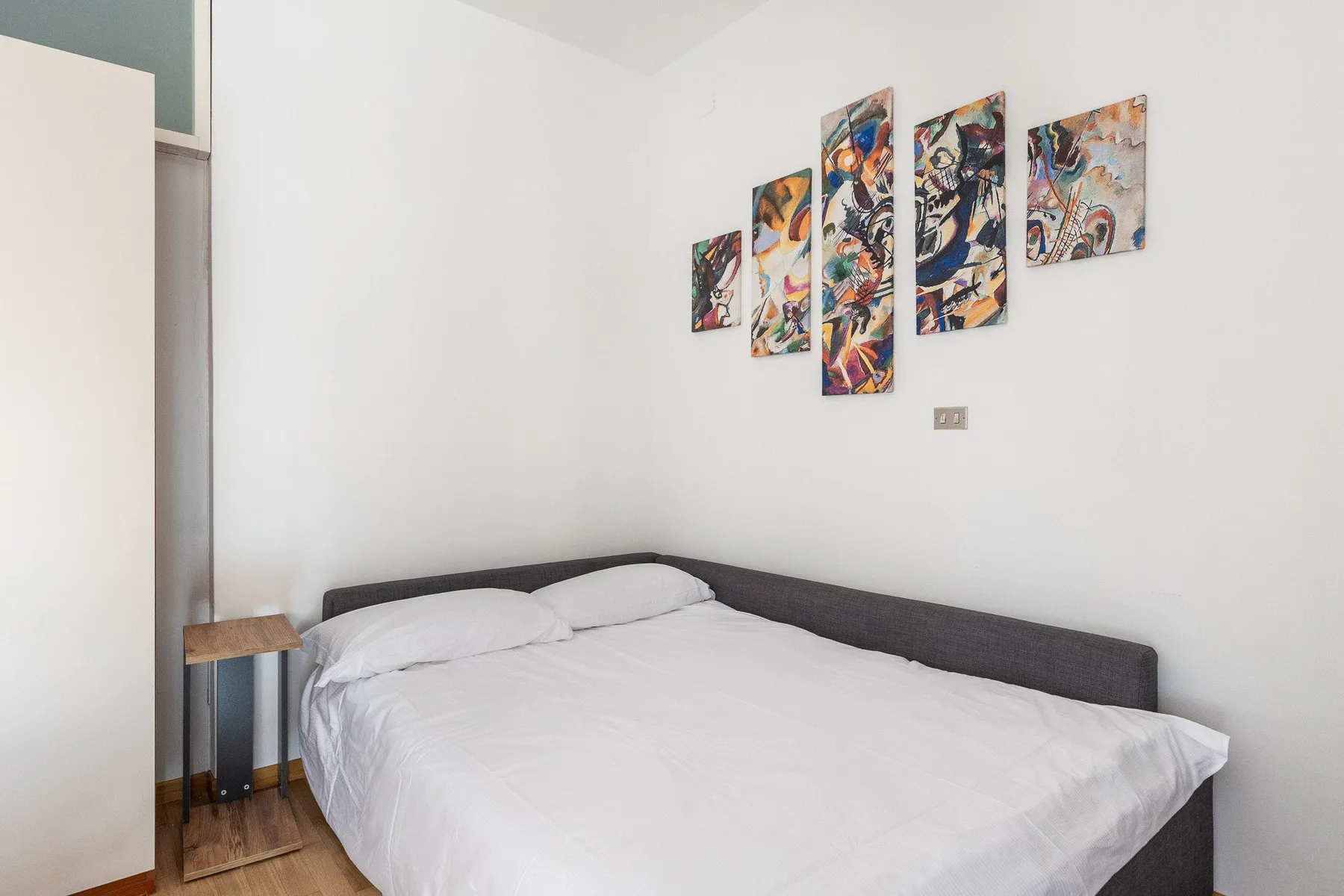 A bedroom with a neatly made bed and colorful artwork on the wall.