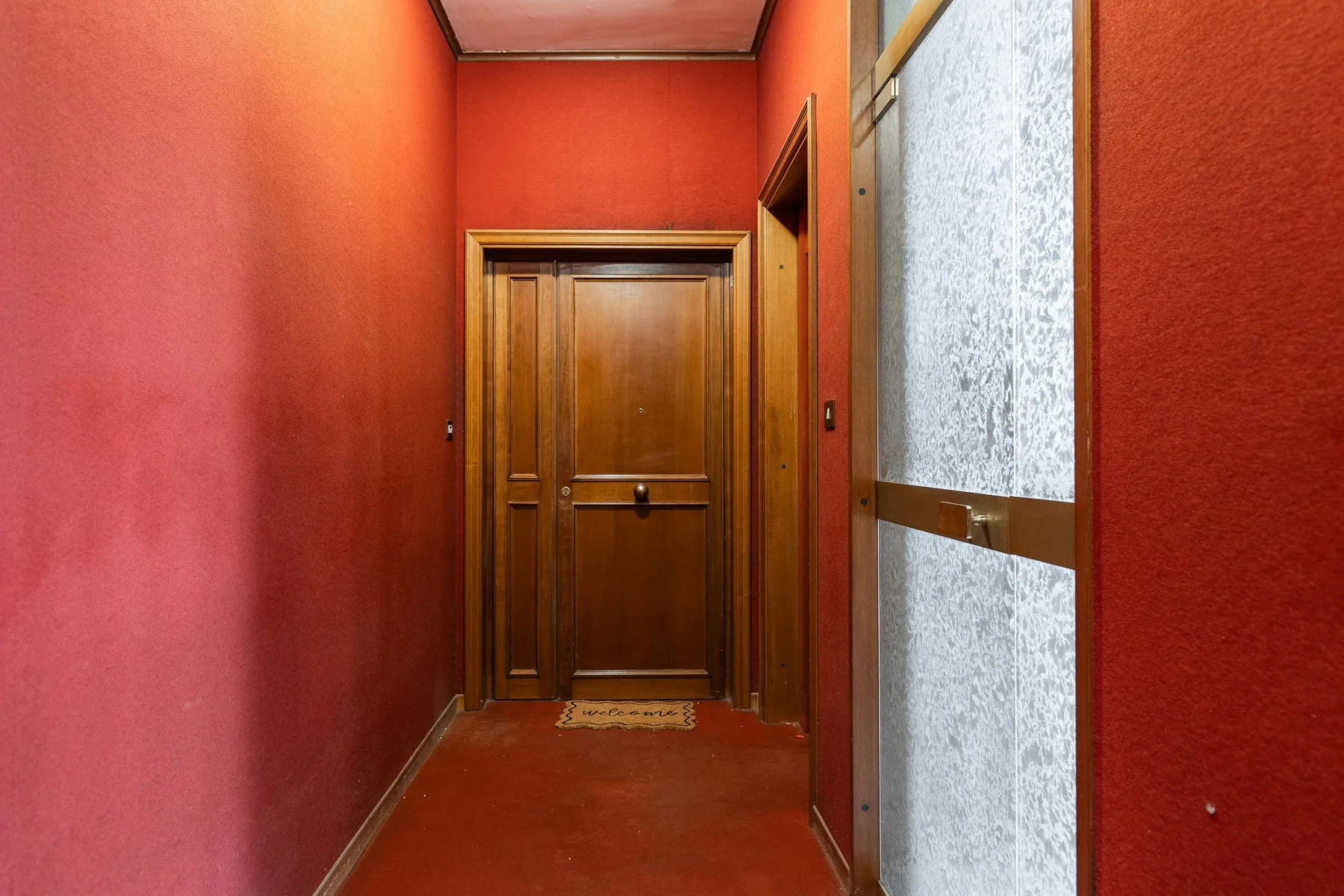 A red hallway leads to a wooden door, with a frosted glass panel beside it.