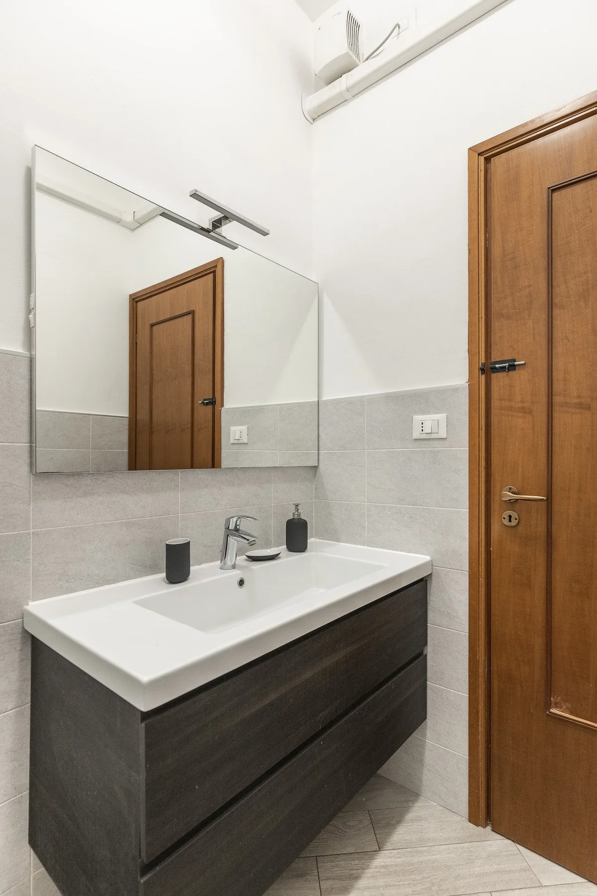 A bathroom vanity with a white basin, wall mirror, and wooden door.