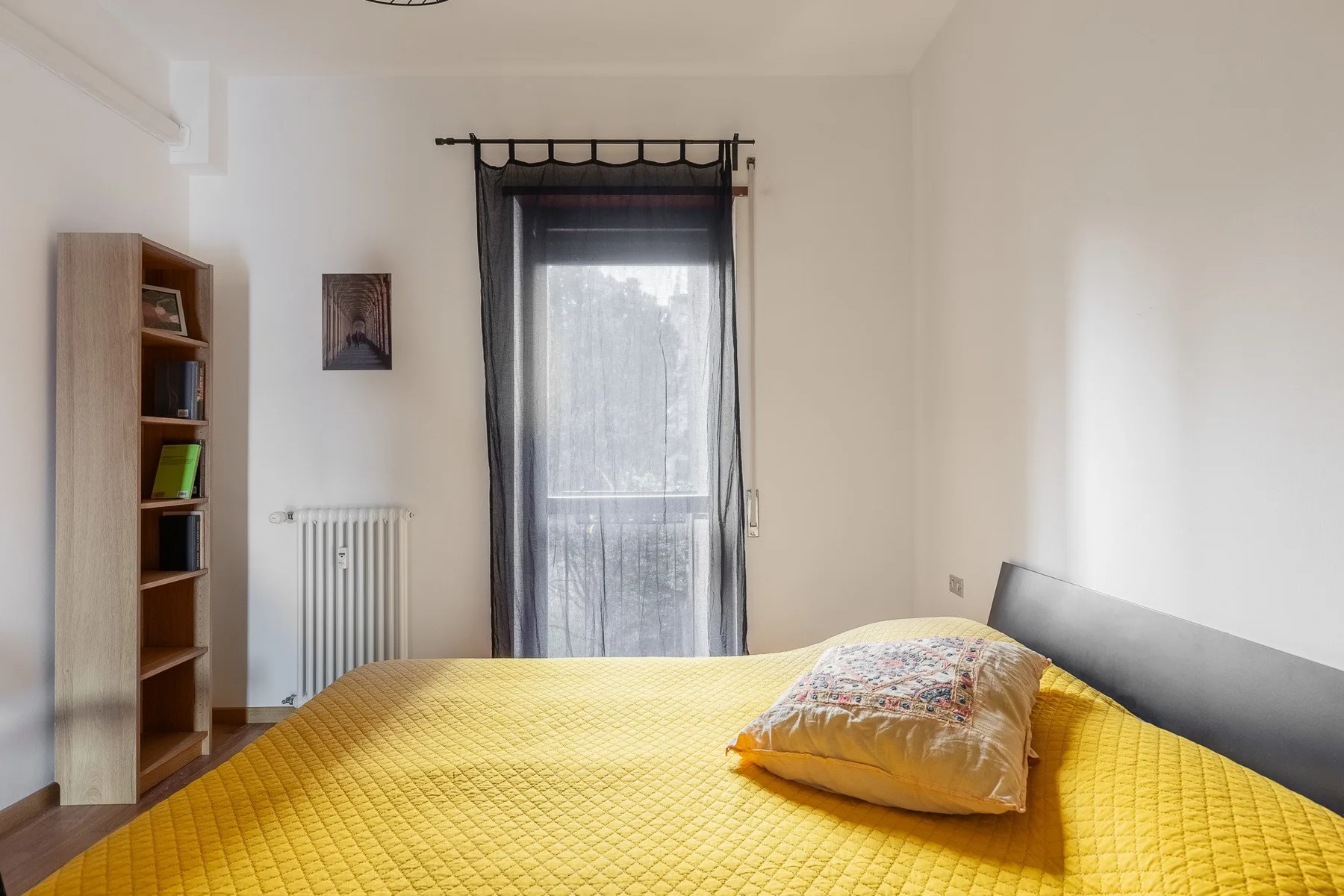 A bedroom with a yellow bedspread and a curtained window.