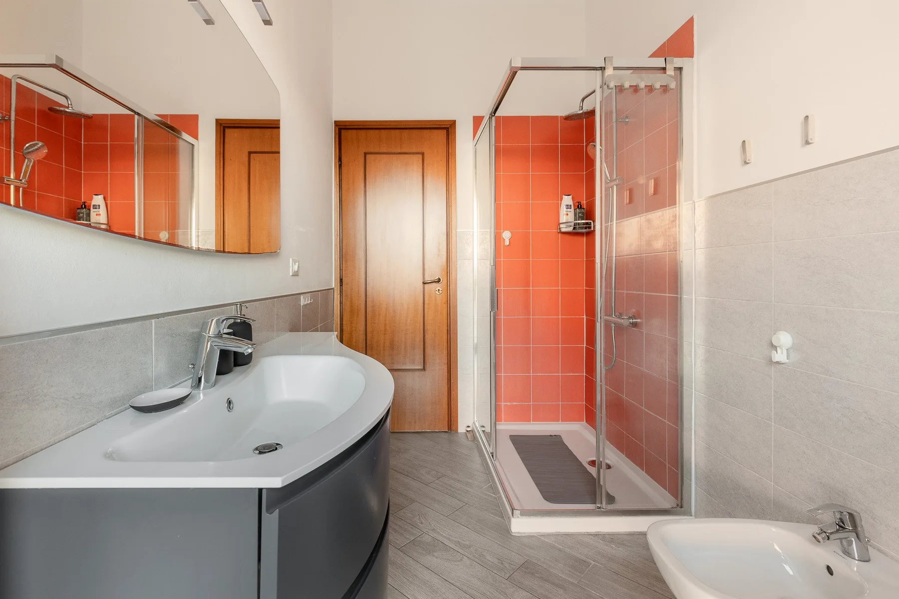 A bathroom with a curved sink, mirror, and glass shower.