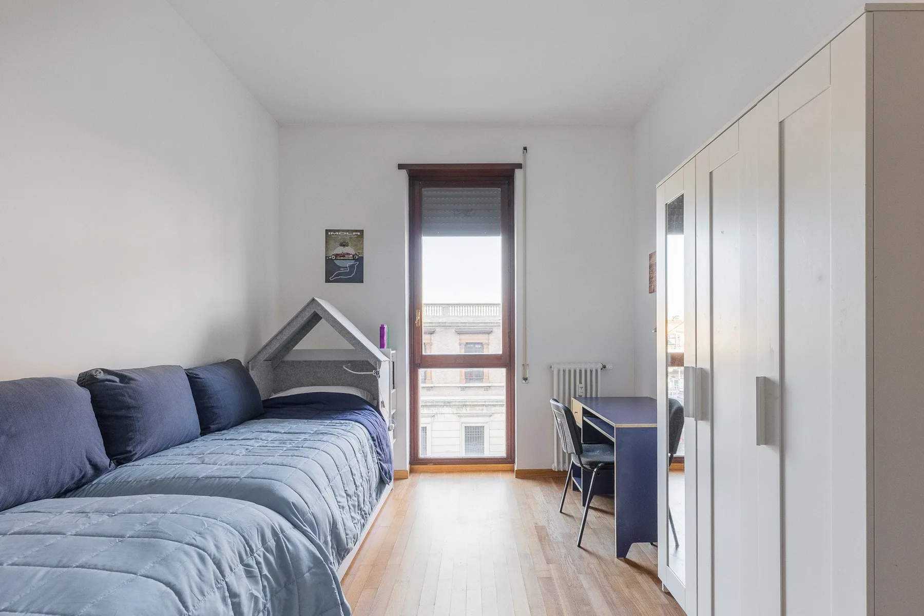A bedroom with a bed, a desk, and a window at the far end.