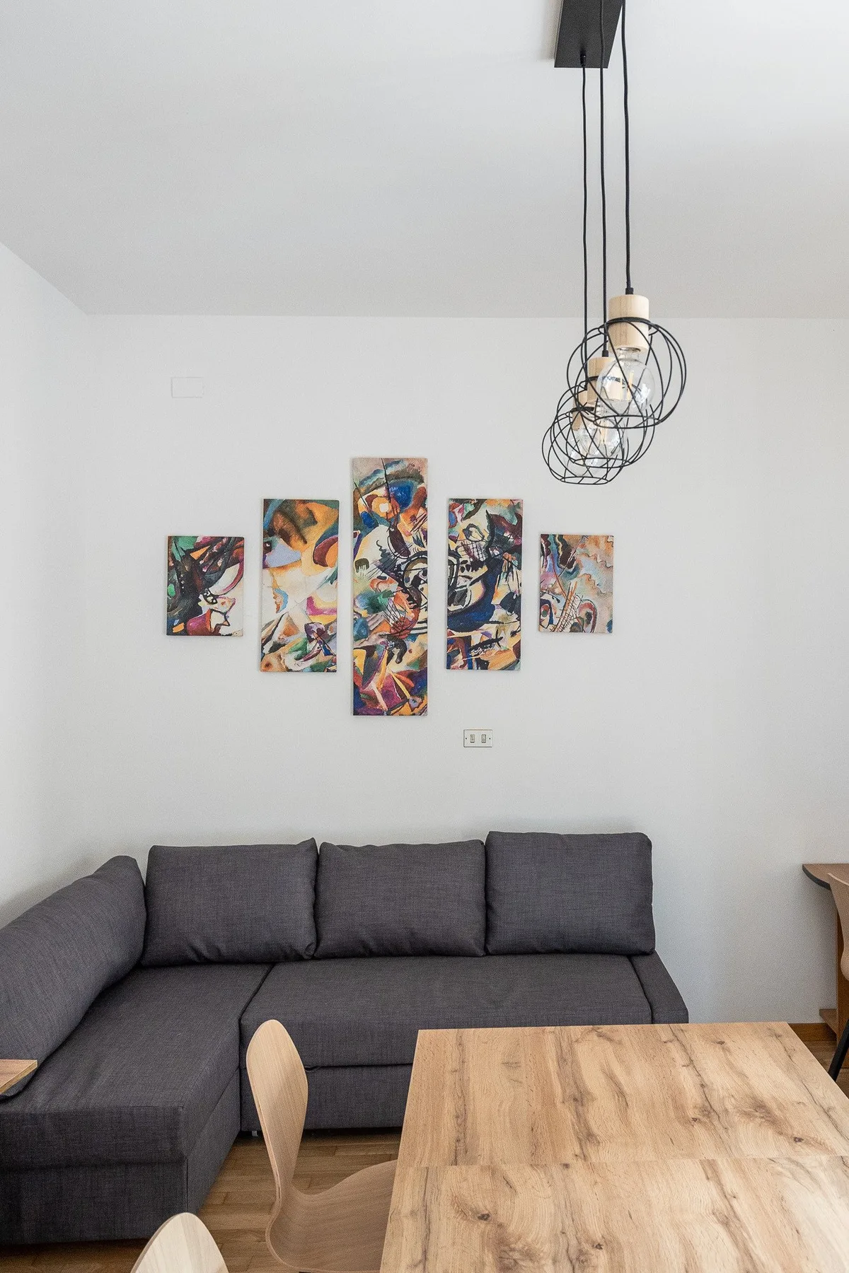 A living room with a dark sectional sofa, wooden coffee table, and colorful wall art.