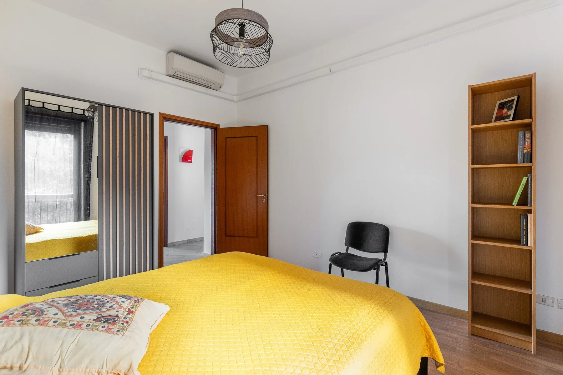 A bedroom with a yellow bed, a wardrobe, and a wooden bookshelf.