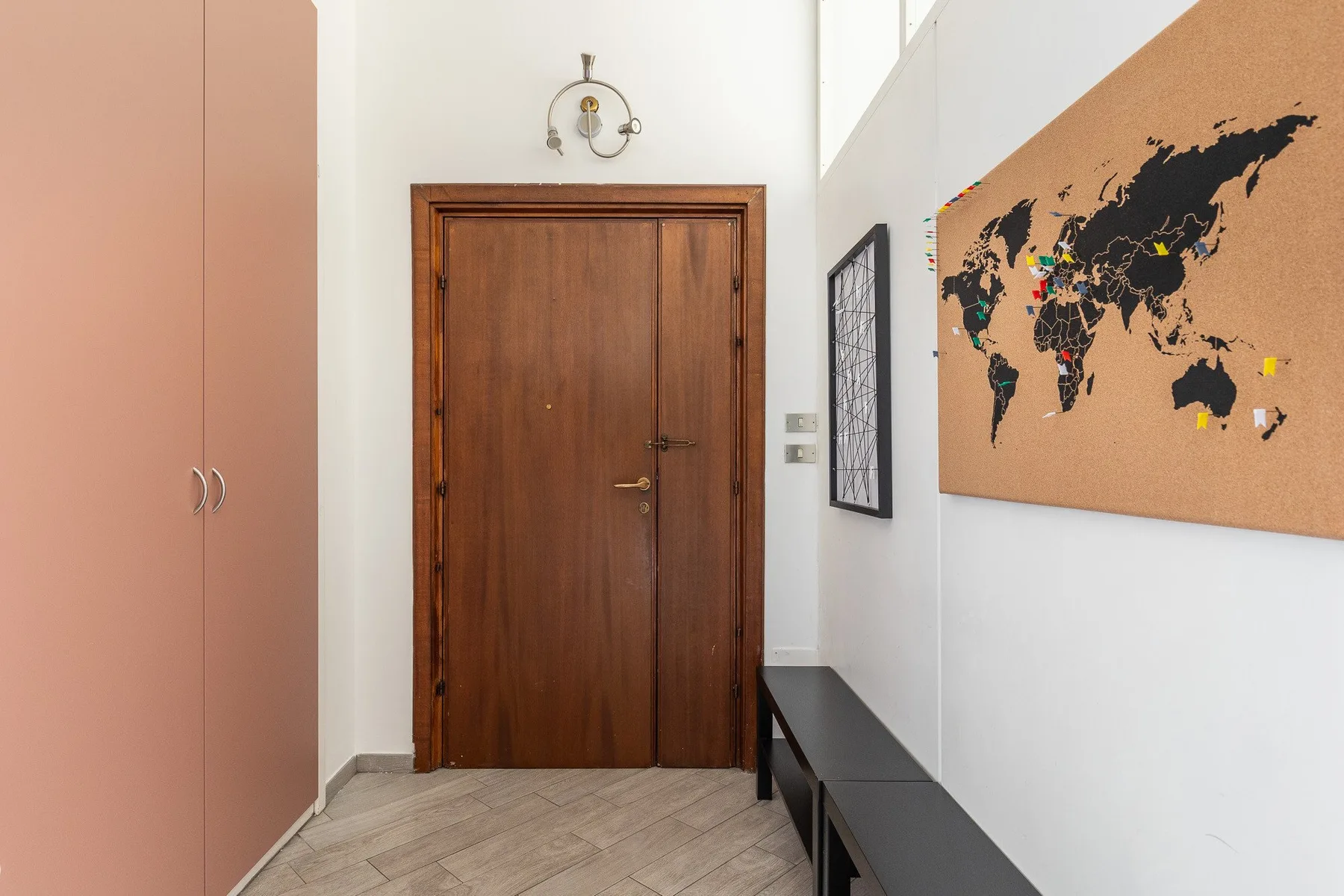 An interior hallway with a wooden door, a wall map, and a bench.