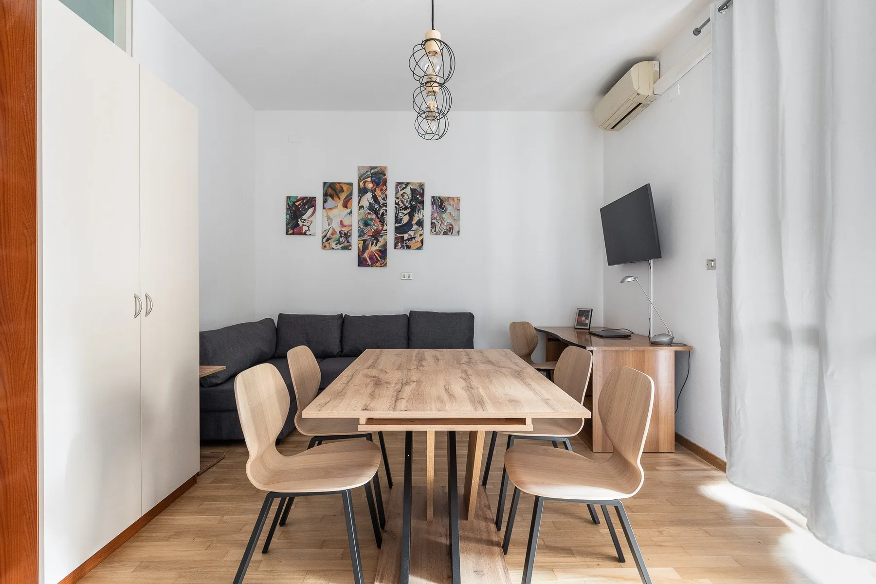 A dining table and chairs sit in a bright room with a dark seating area.