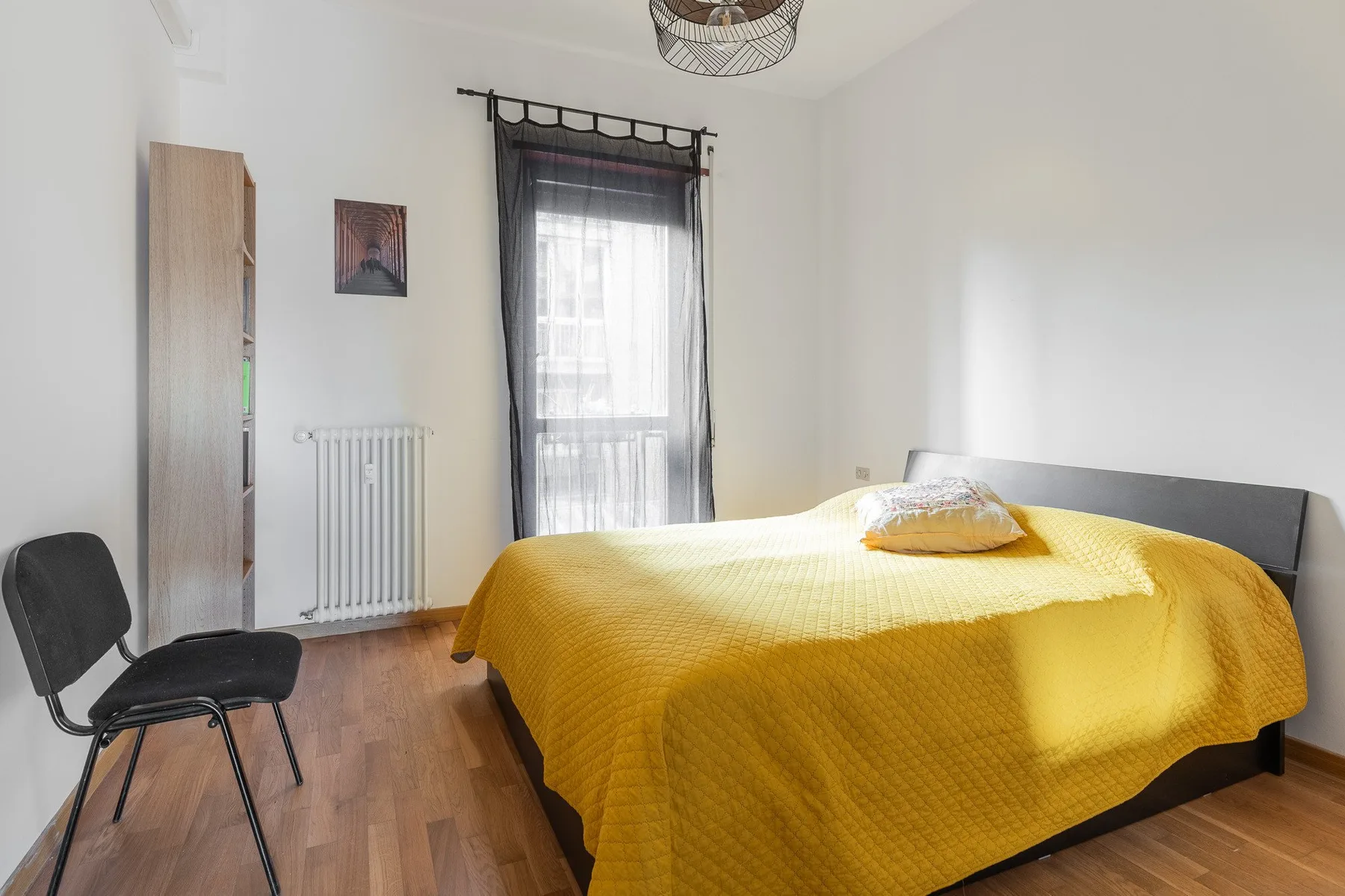 A bedroom with a bed covered in a bright yellow bedspread beside a curtained window.