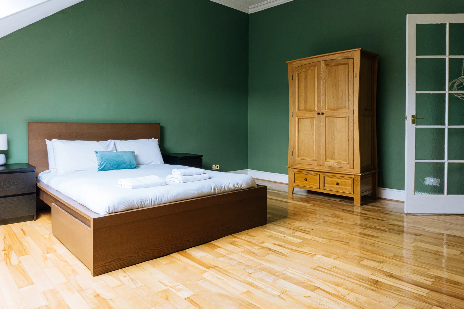 Un dormitorio con una cama y un armario de madera junto a paredes verde oscuro.