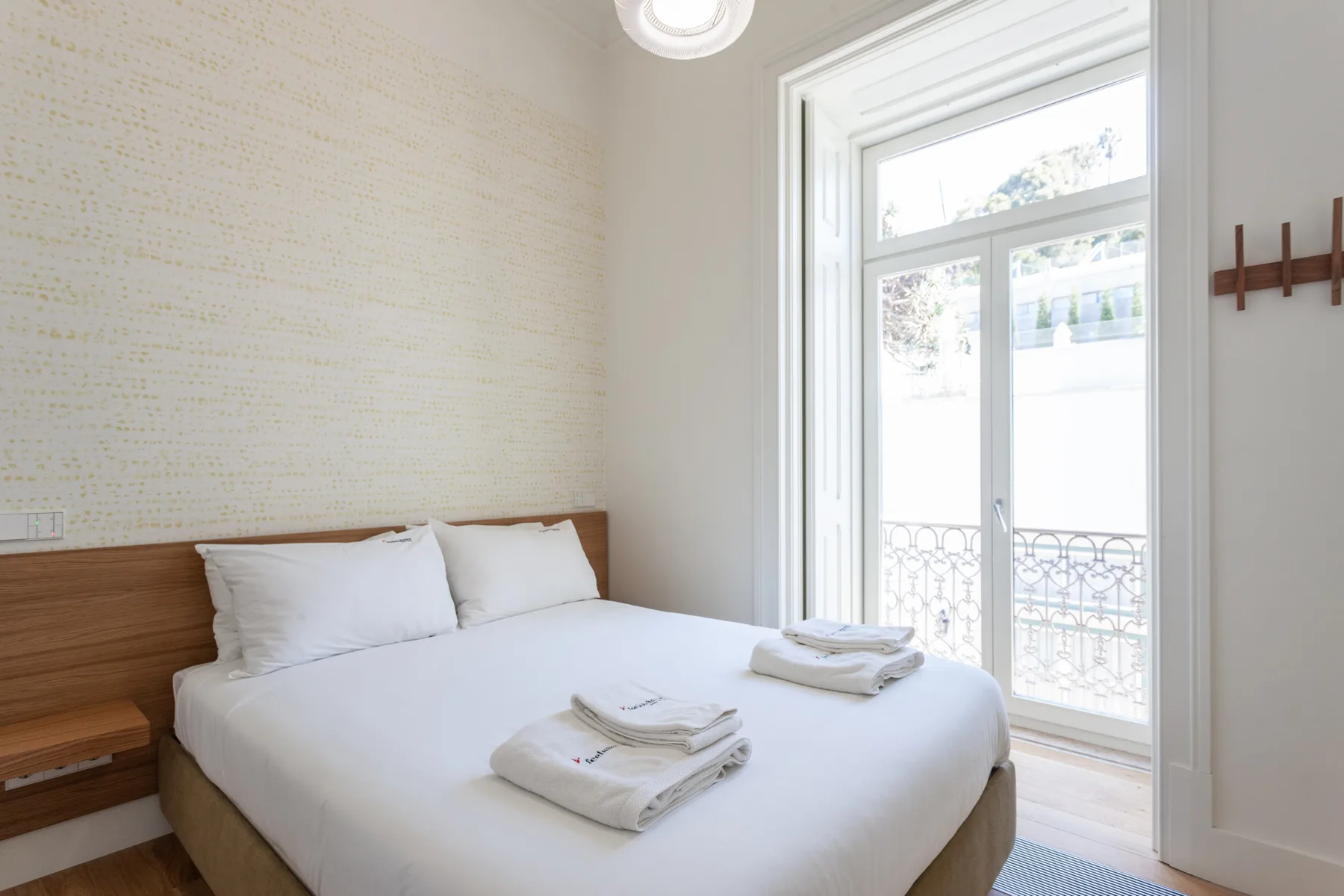 Un dormitorio luminoso con una cama bien tendida junto a una ventana alta.