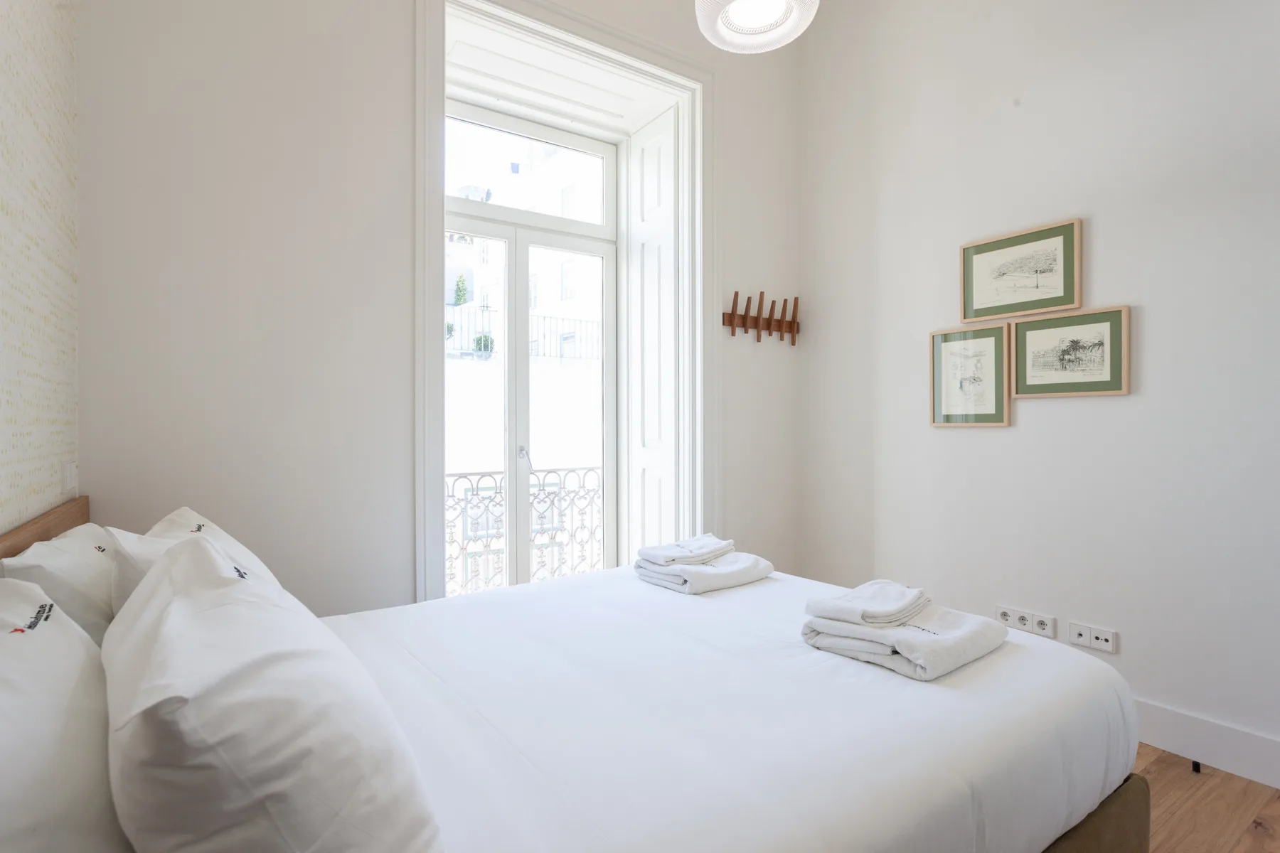 Un dormitorio luminoso con una cama bien hecha junto a una ventana alta.