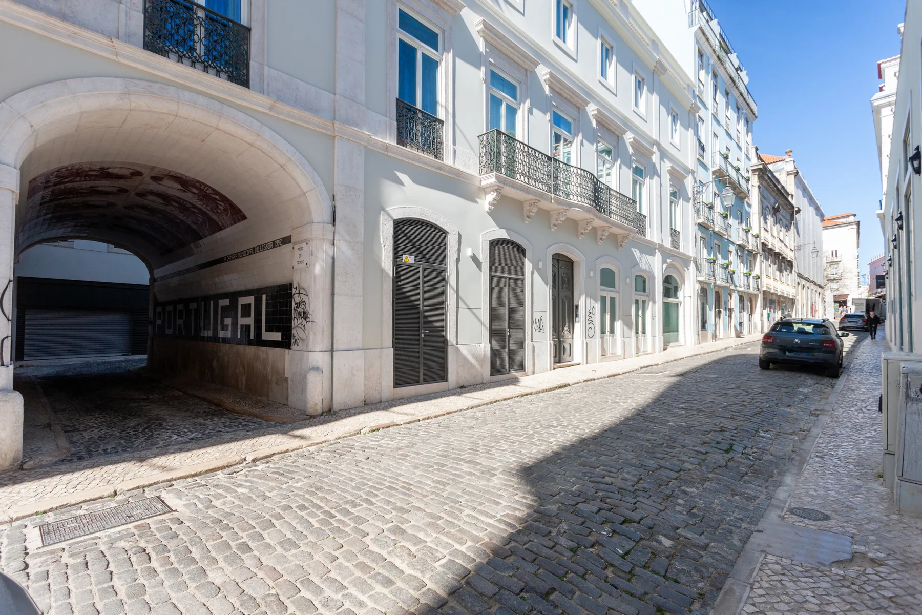 Una calle empedrada pasa junto a edificios claros con ventanas cerradas.