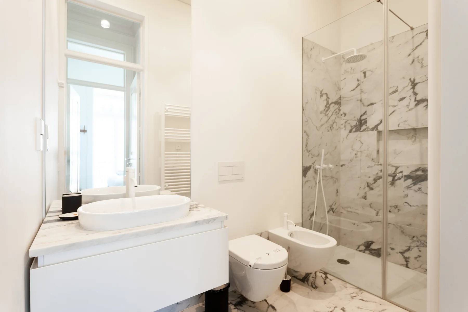 Un baño luminoso con lavabo, inodoro, bidé y ducha de cristal.