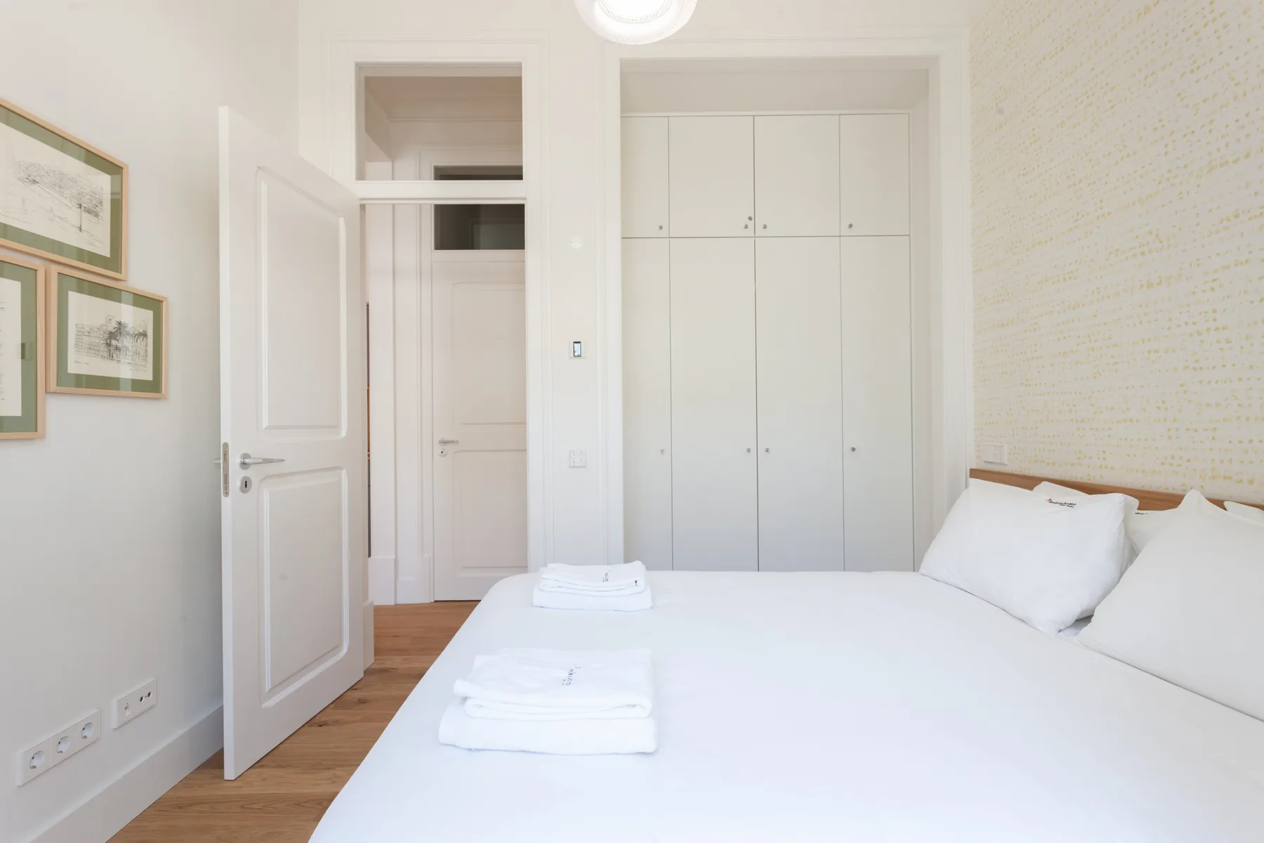 Un dormitorio luminoso con ropa de cama blanca, armarios empotrados y una puerta abierta.