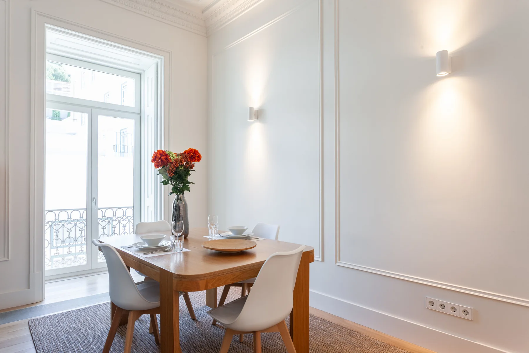 Un comedor con una mesa de madera y sillas junto a una ventana alta.