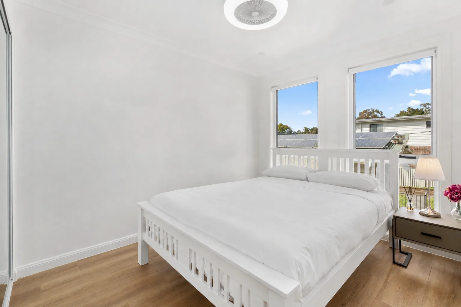 Un dormitorio luminoso con una cama blanca junto a dos ventanas.