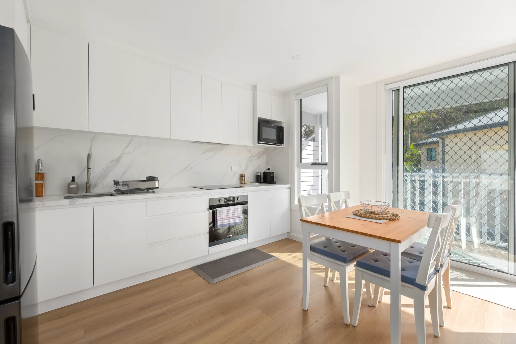 Una cocina luminosa con armarios blancos y una mesa de comedor junto a una puerta corrediza de vidrio.