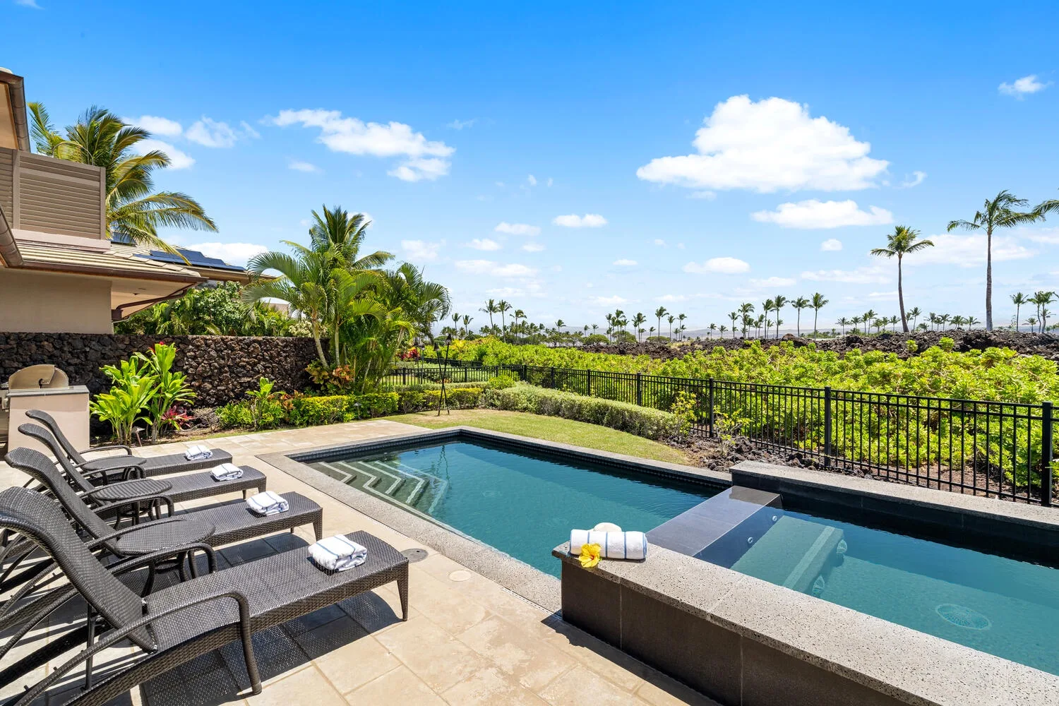 Una piscina exterior junto a asientos reclinables y un jardín.