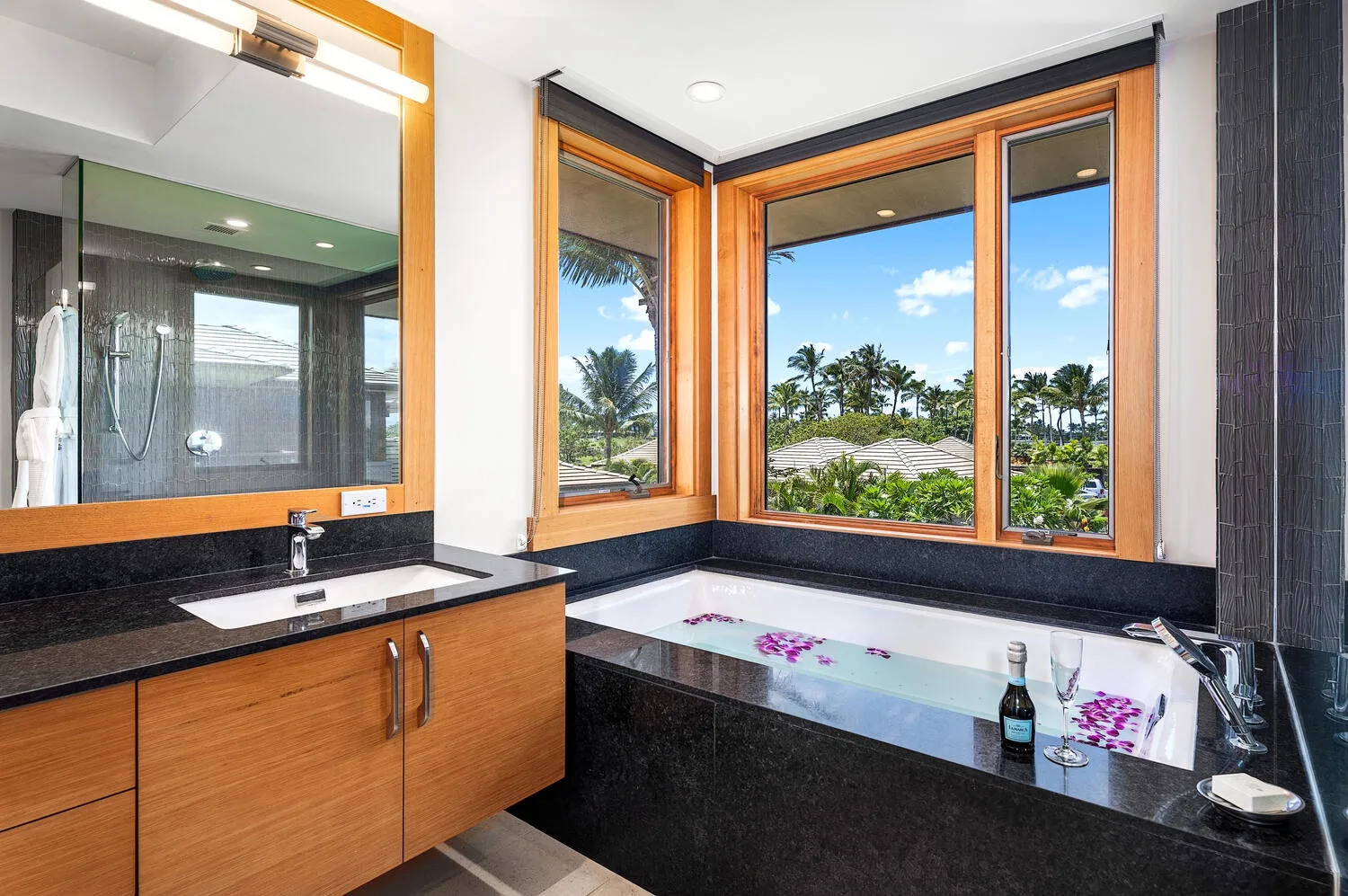 Un baño con una bañera junto a grandes ventanas con vista a palmeras.