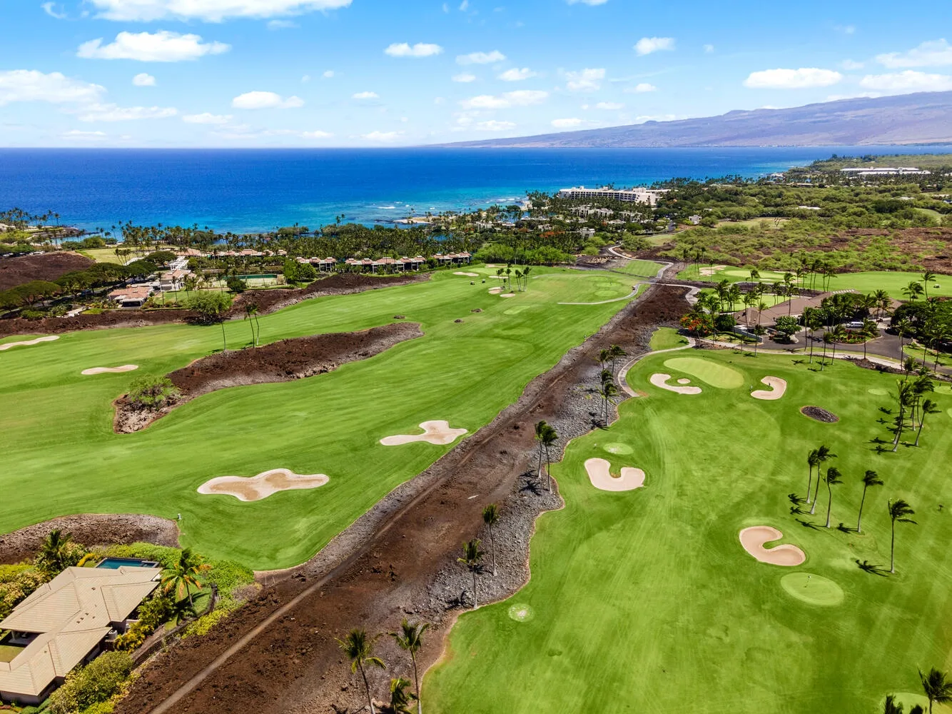 Vista aérea de un campo de golf con el océano y la costa al fondo.