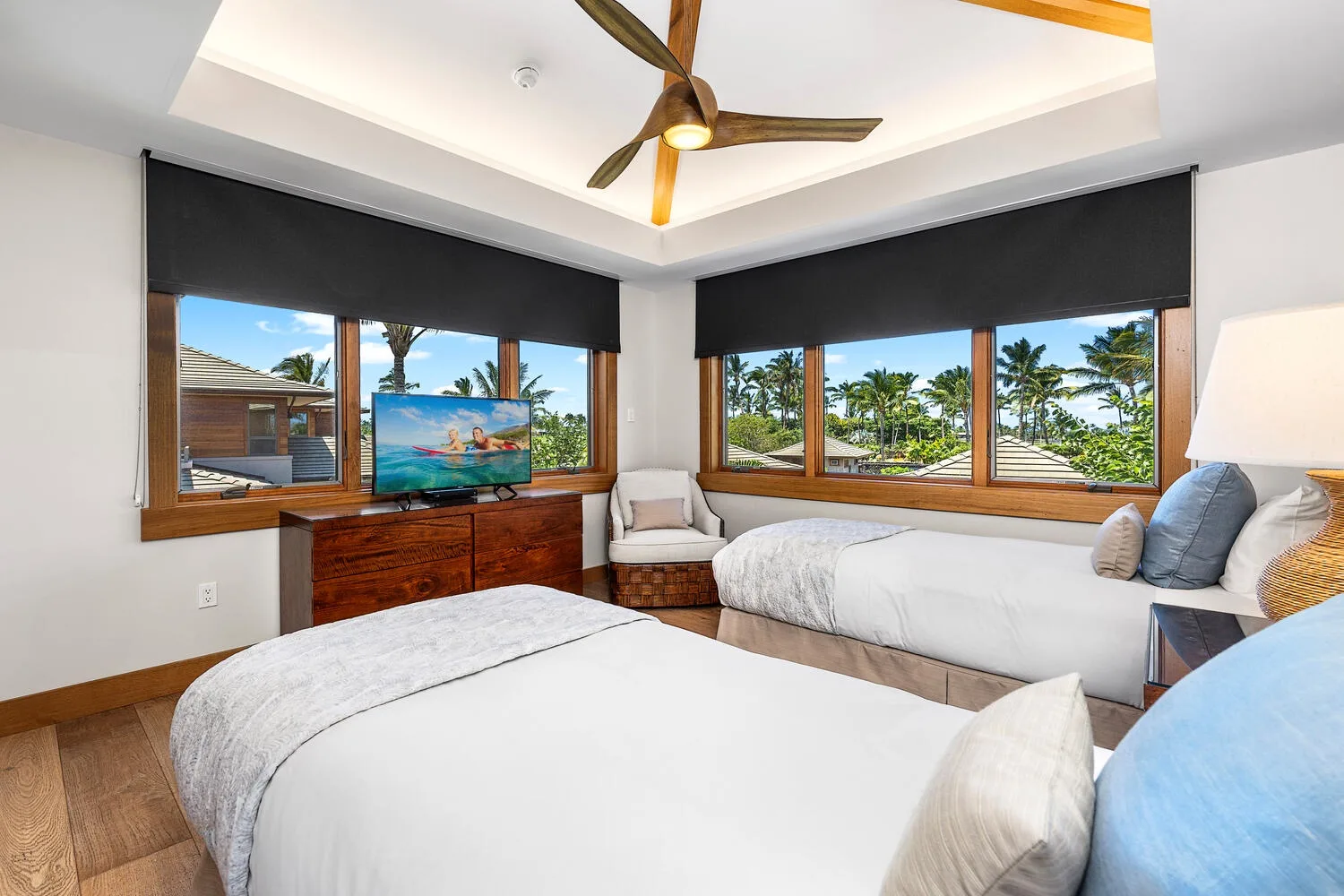 Un dormitorio luminoso con dos camas y grandes ventanas con vistas a palmeras.