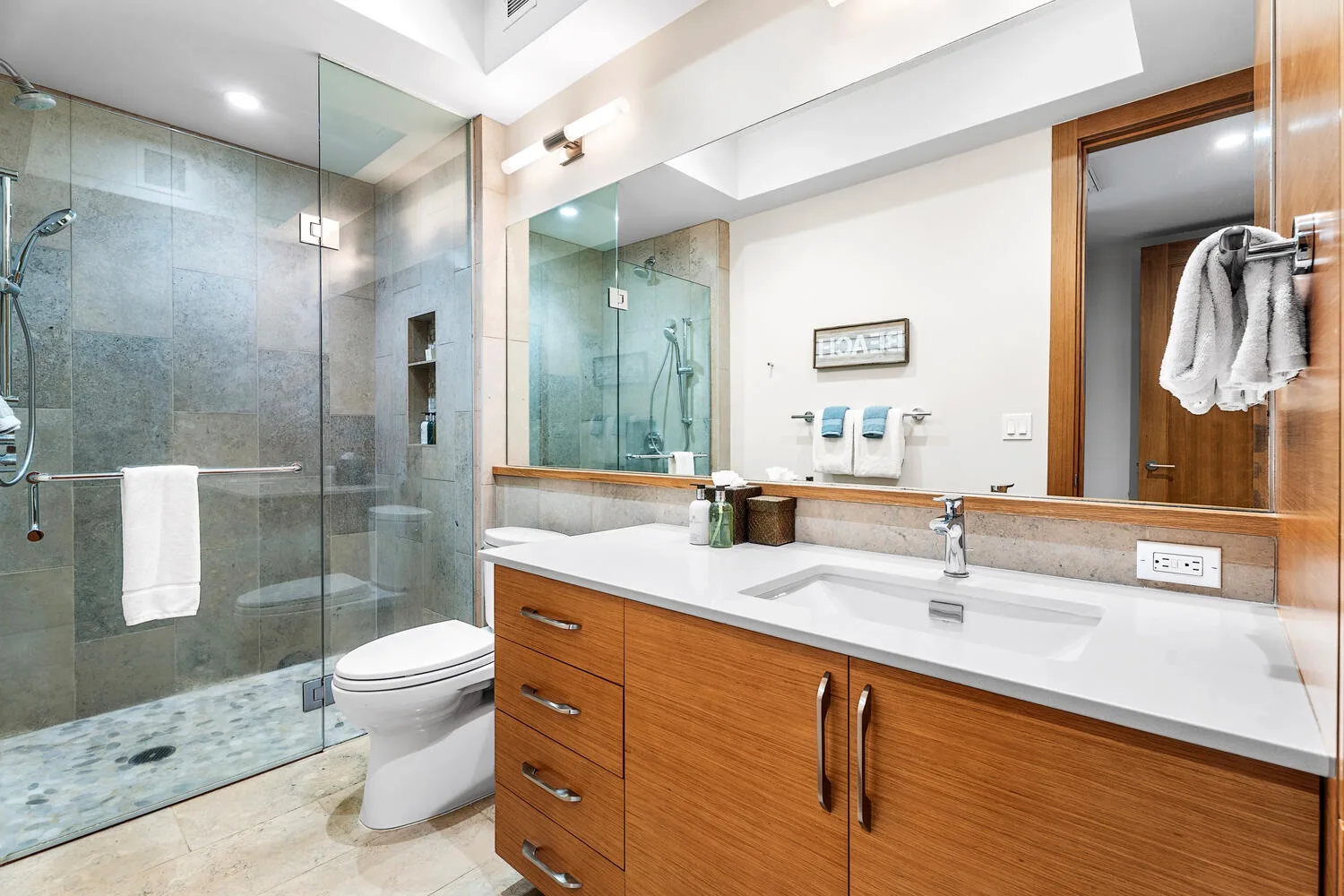 Un baño con ducha de vidrio, inodoro y tocador de madera.