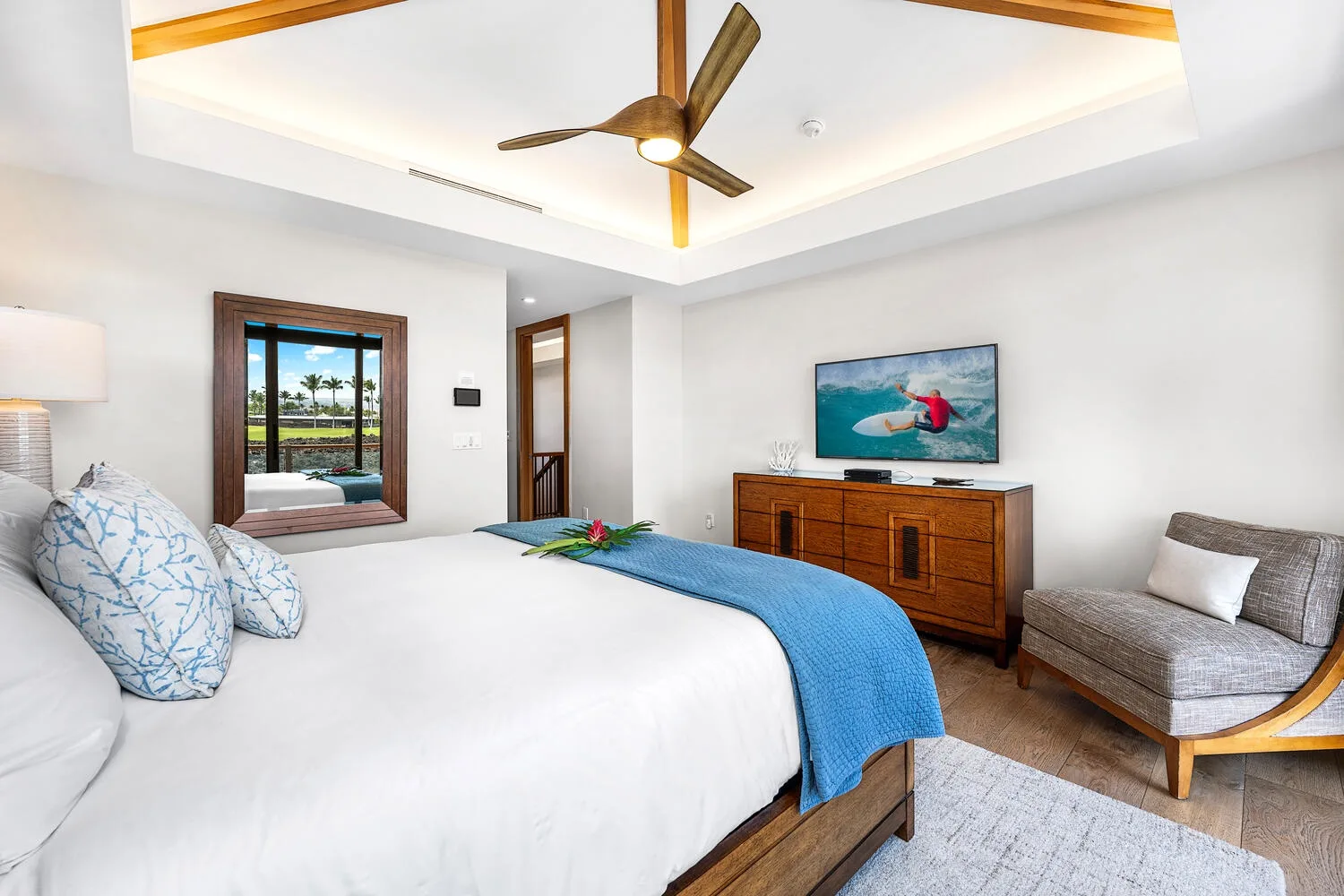 Un dormitorio luminoso con una cama tendida y un televisor sobre una cómoda de madera.