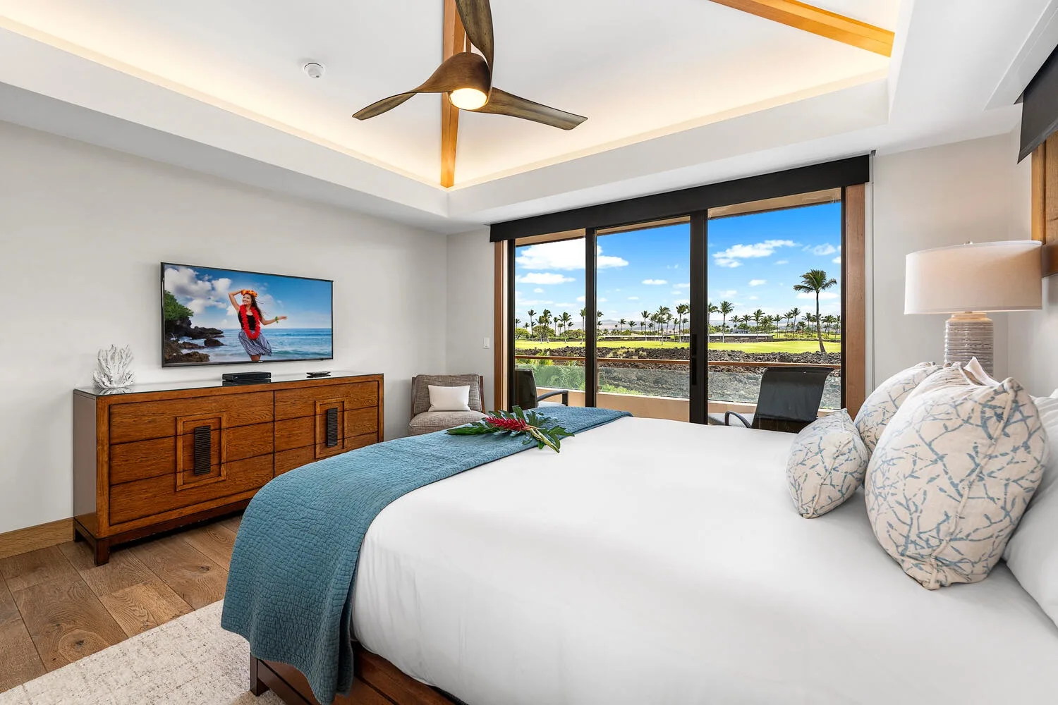 Un dormitorio luminoso con una cama frente a grandes ventanas y palmeras a la vista.