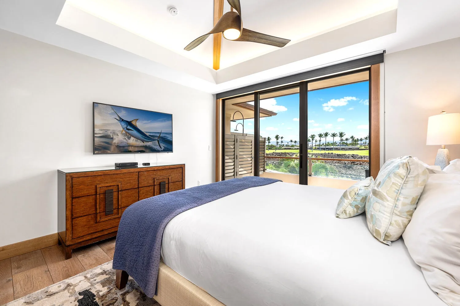 Un dormitorio luminoso con una cama frente a una gran ventana con palmeras a la vista.