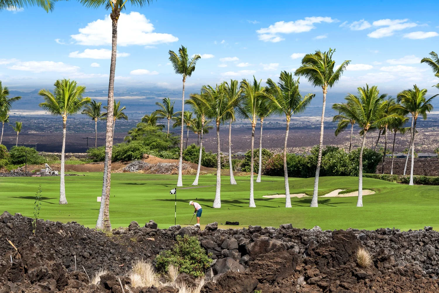 Un campo de golf ajardinado con palmeras y una persona cuidando el césped.