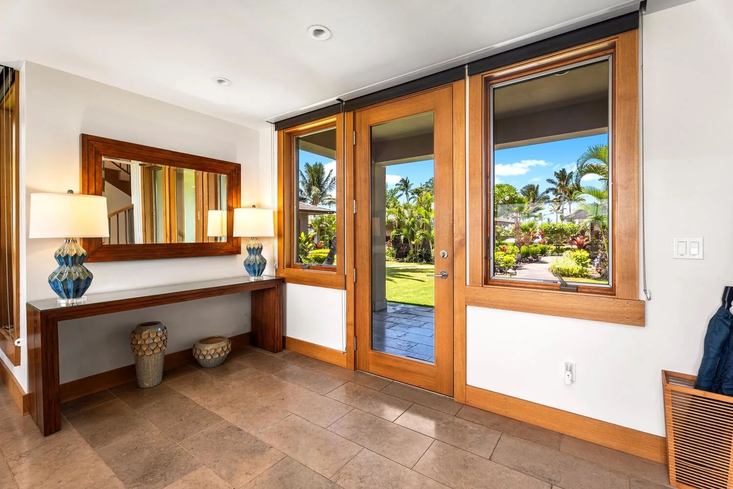 Una entrada con una consola de madera y grandes ventanas con vistas a un jardín.
