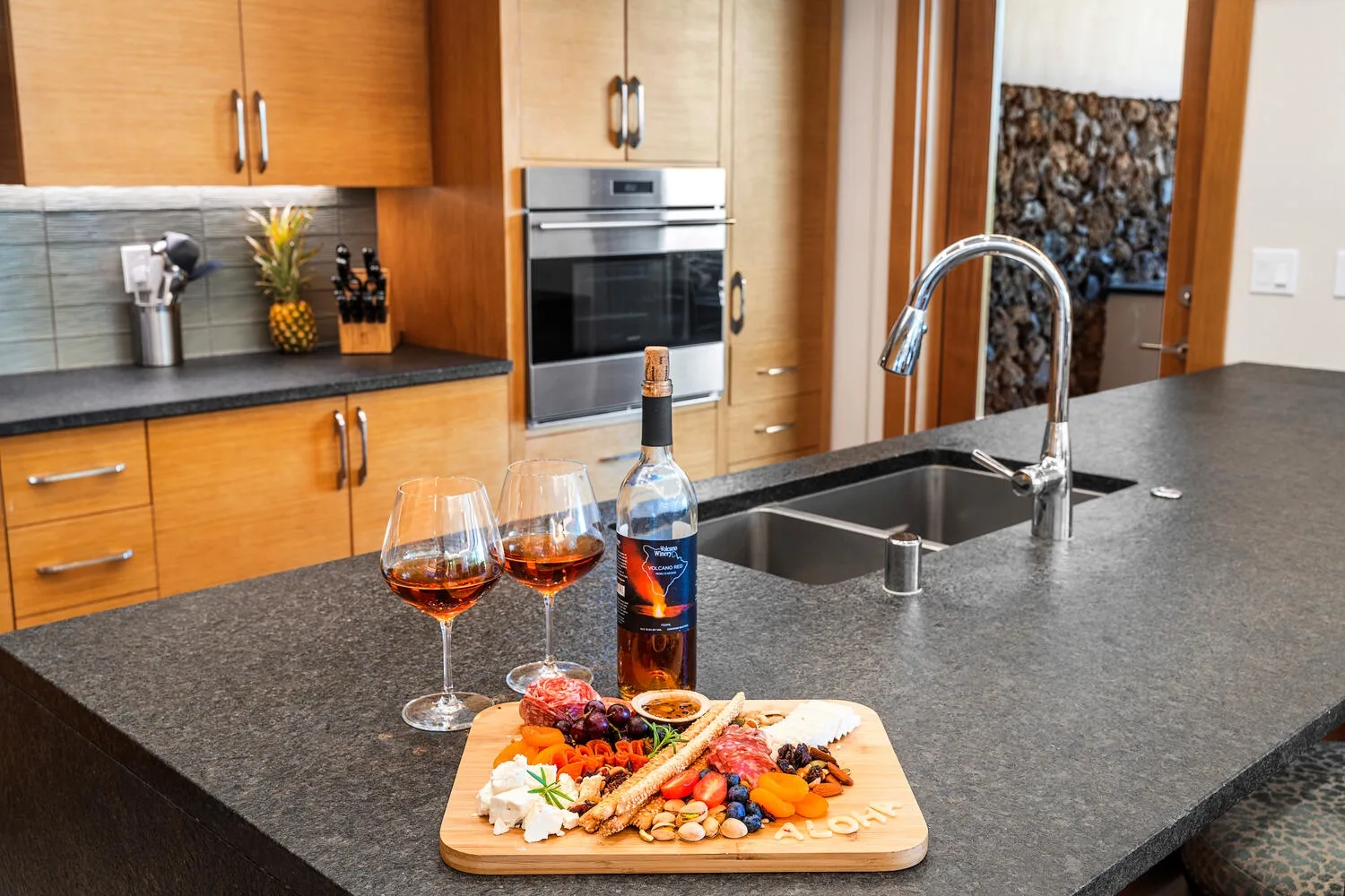 Una isla de cocina exhibe una tabla con comida y copas de vino.