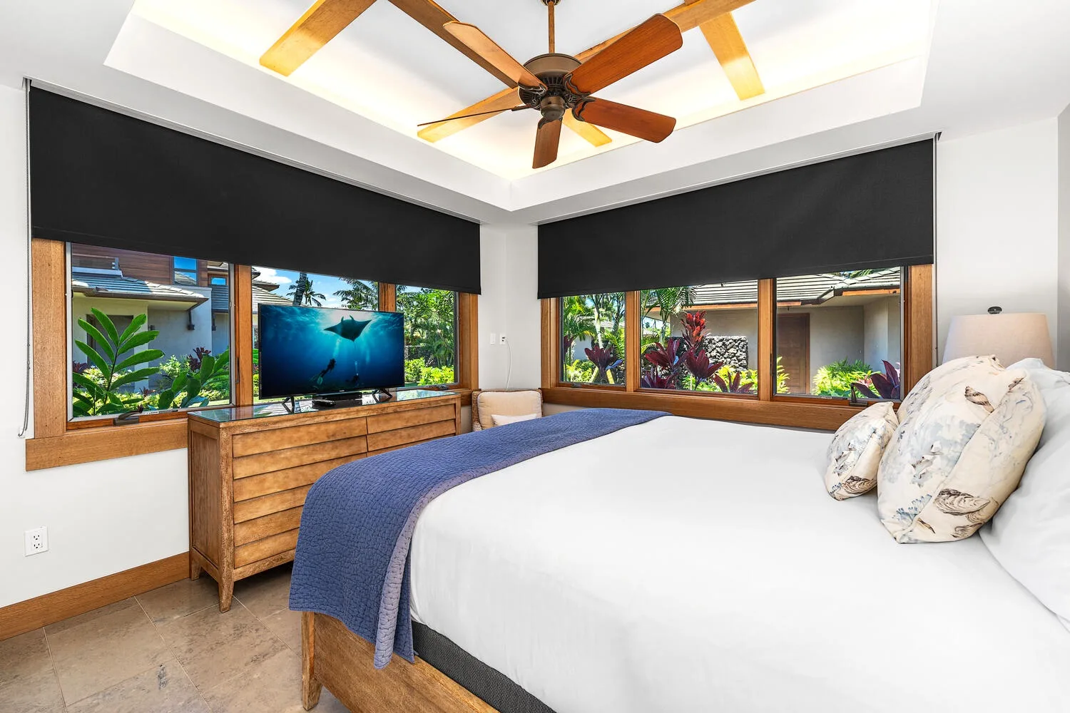 Un dormitorio con cama, cómoda de madera y ventanas con vistas a vegetación tropical.