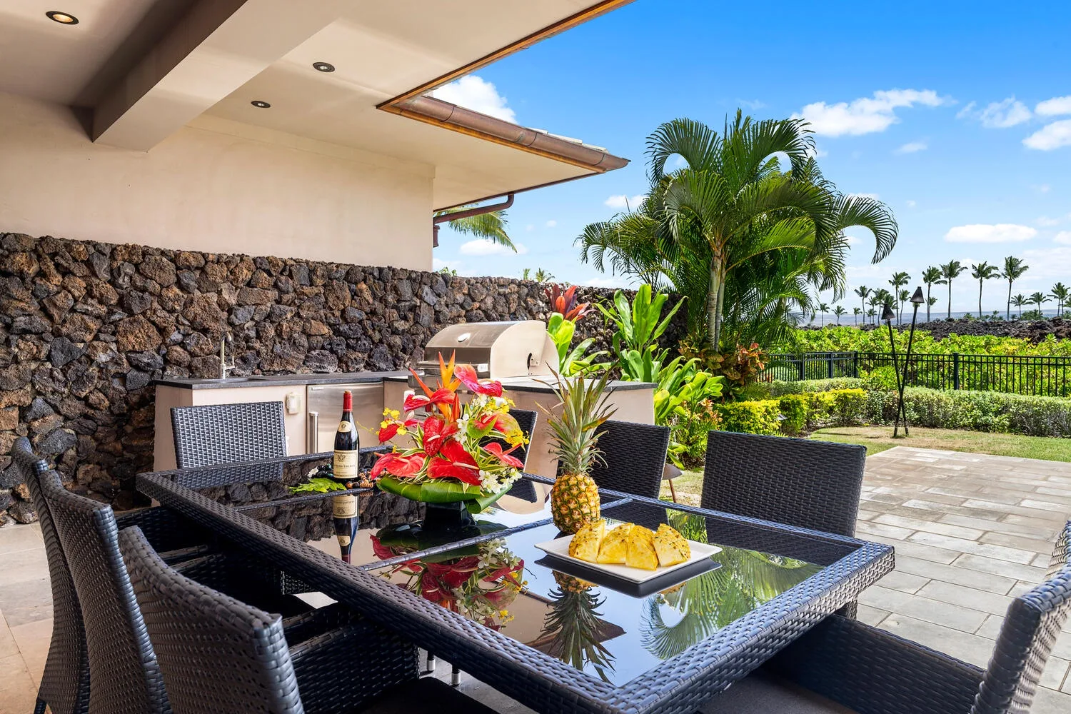 Una zona de comedor al aire libre con una mesa de vidrio y plantas tropicales.
