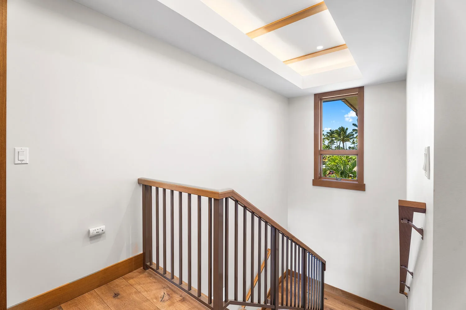 Una escalera luminosa con barandilla de madera y una ventana con vista a la vegetación.