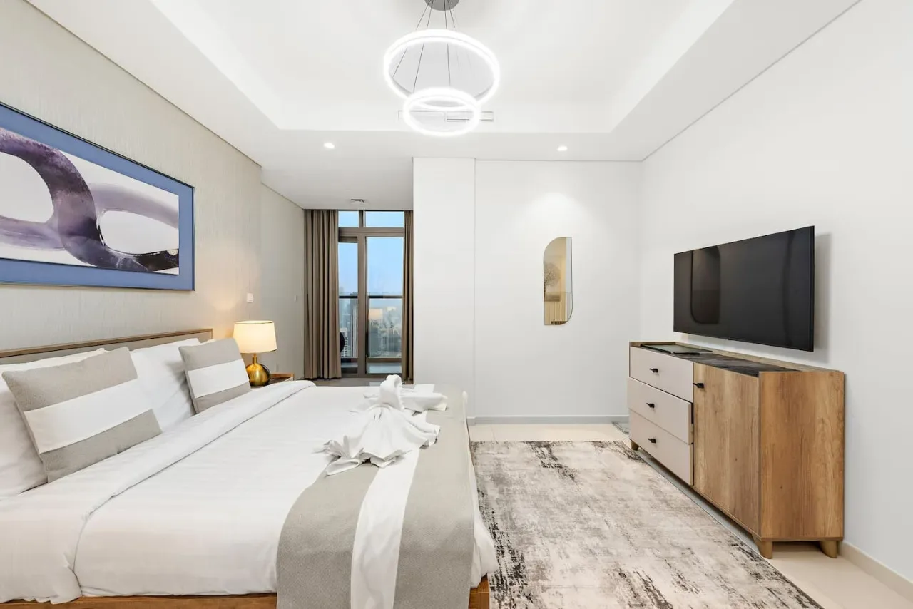 Un dormitorio con una cama tendida, un televisor en la pared y un mueble de madera.