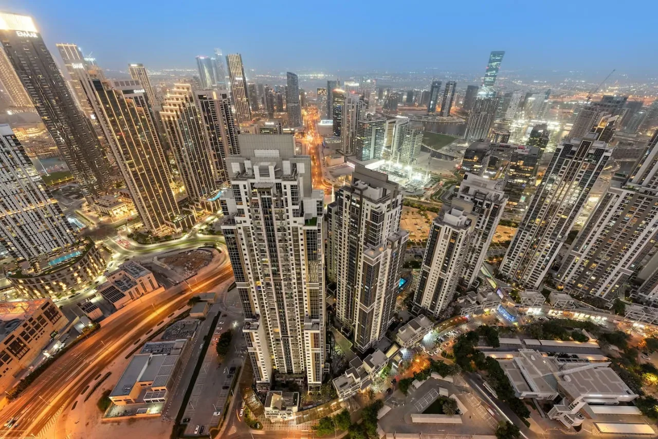 Panorámica aérea de edificios altos y calles iluminadas al anochecer.